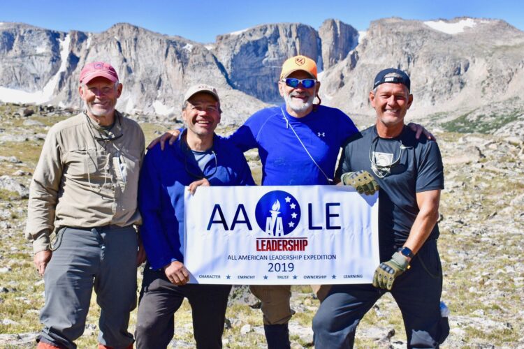 Course participants pose together with the AALE banner in front of rugged peaks of the Wind River Range.