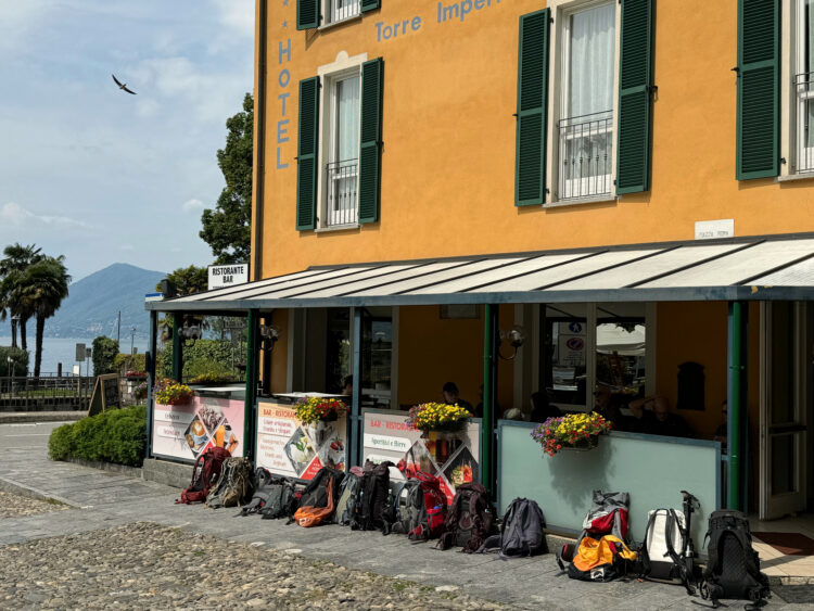 Backpacks laid out in front of a yellow building next to the lake.