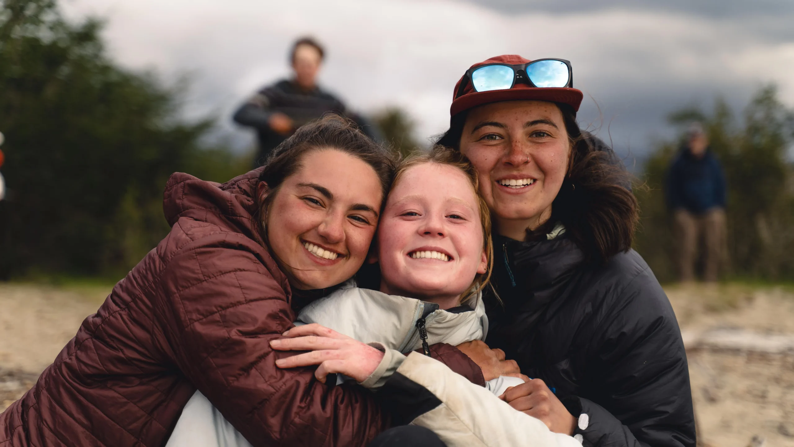 three women smile while embracing.