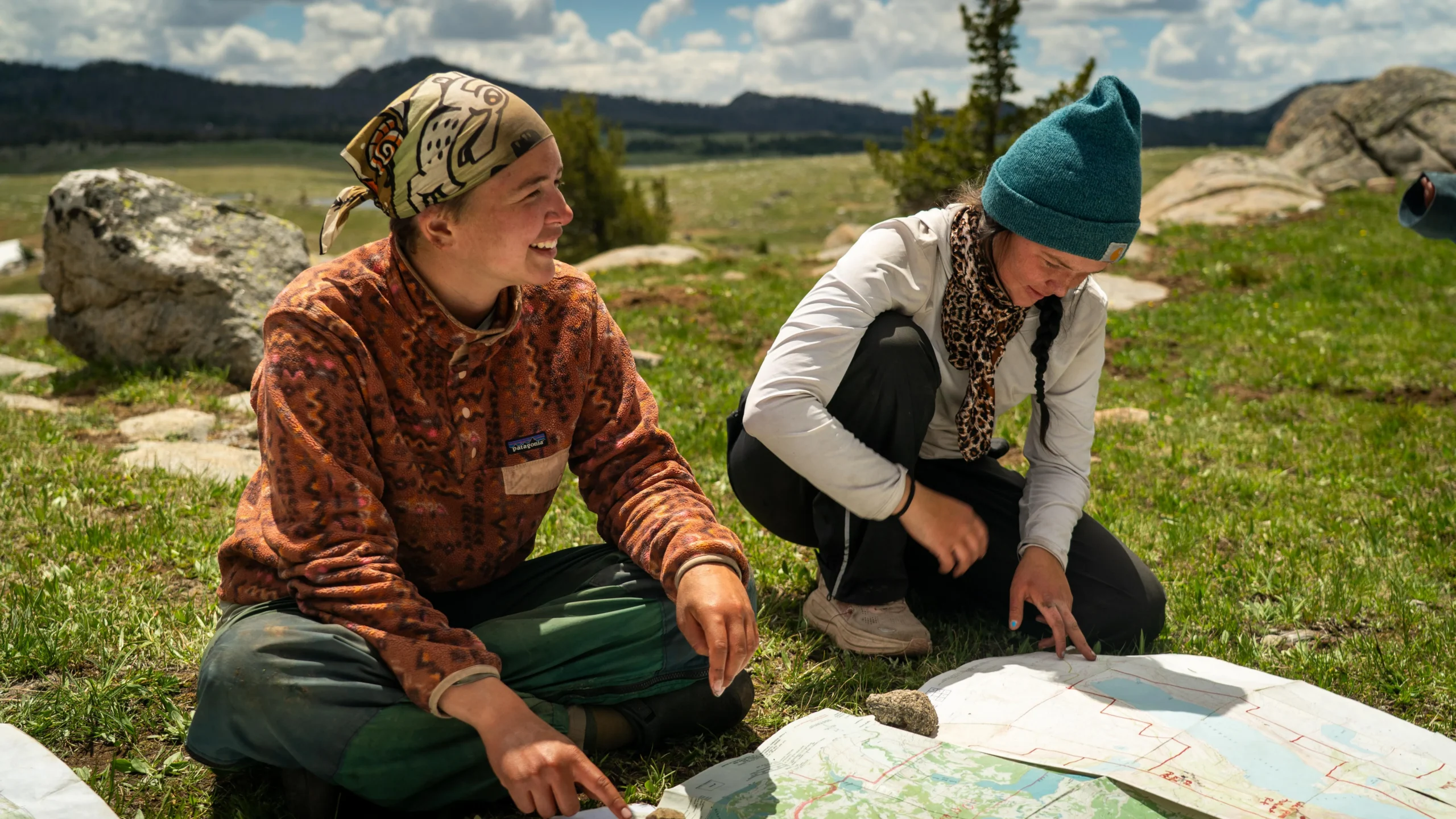 two people look at a map that is on the grass
