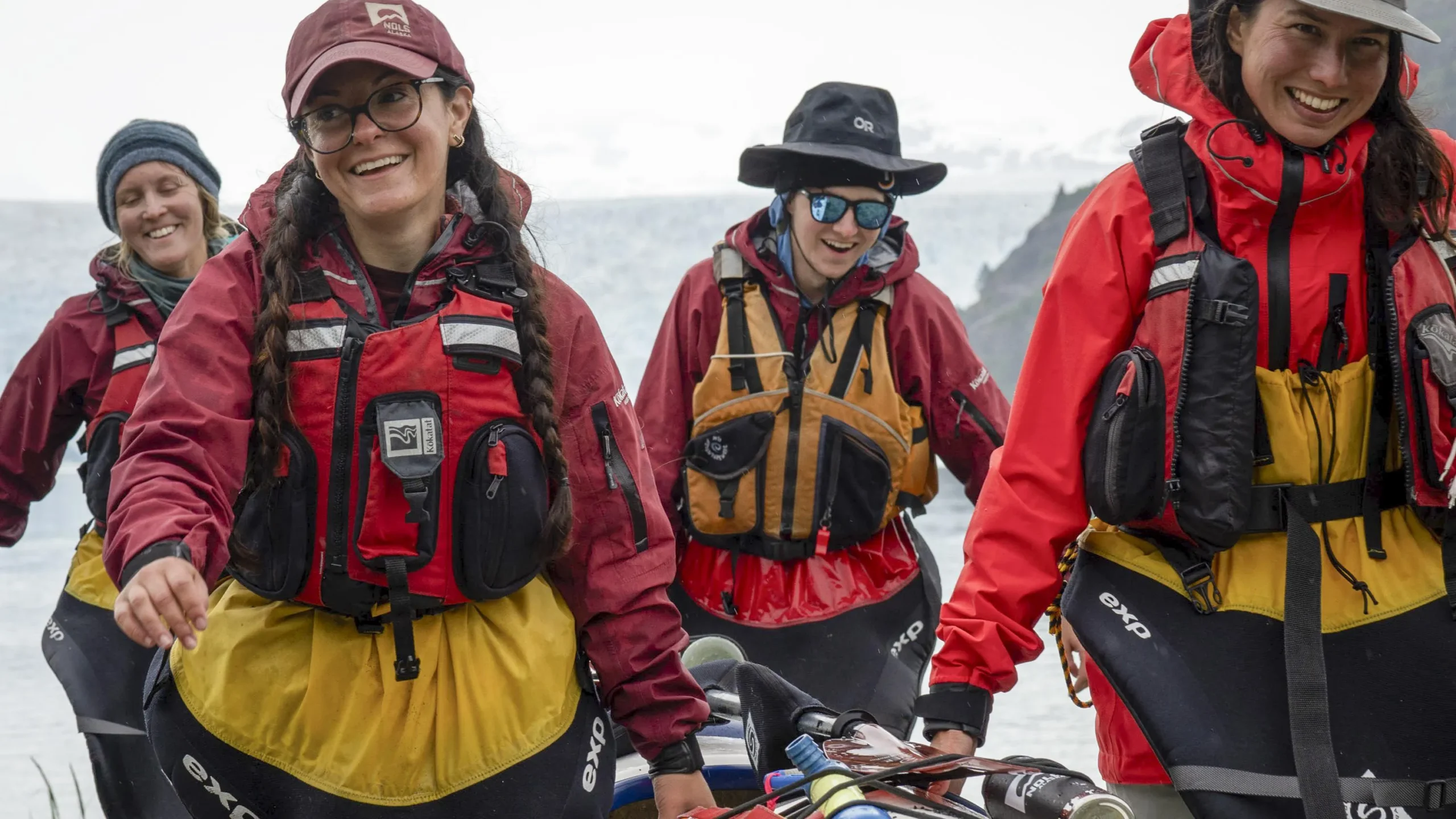 four people in life jackets carry a kayak together