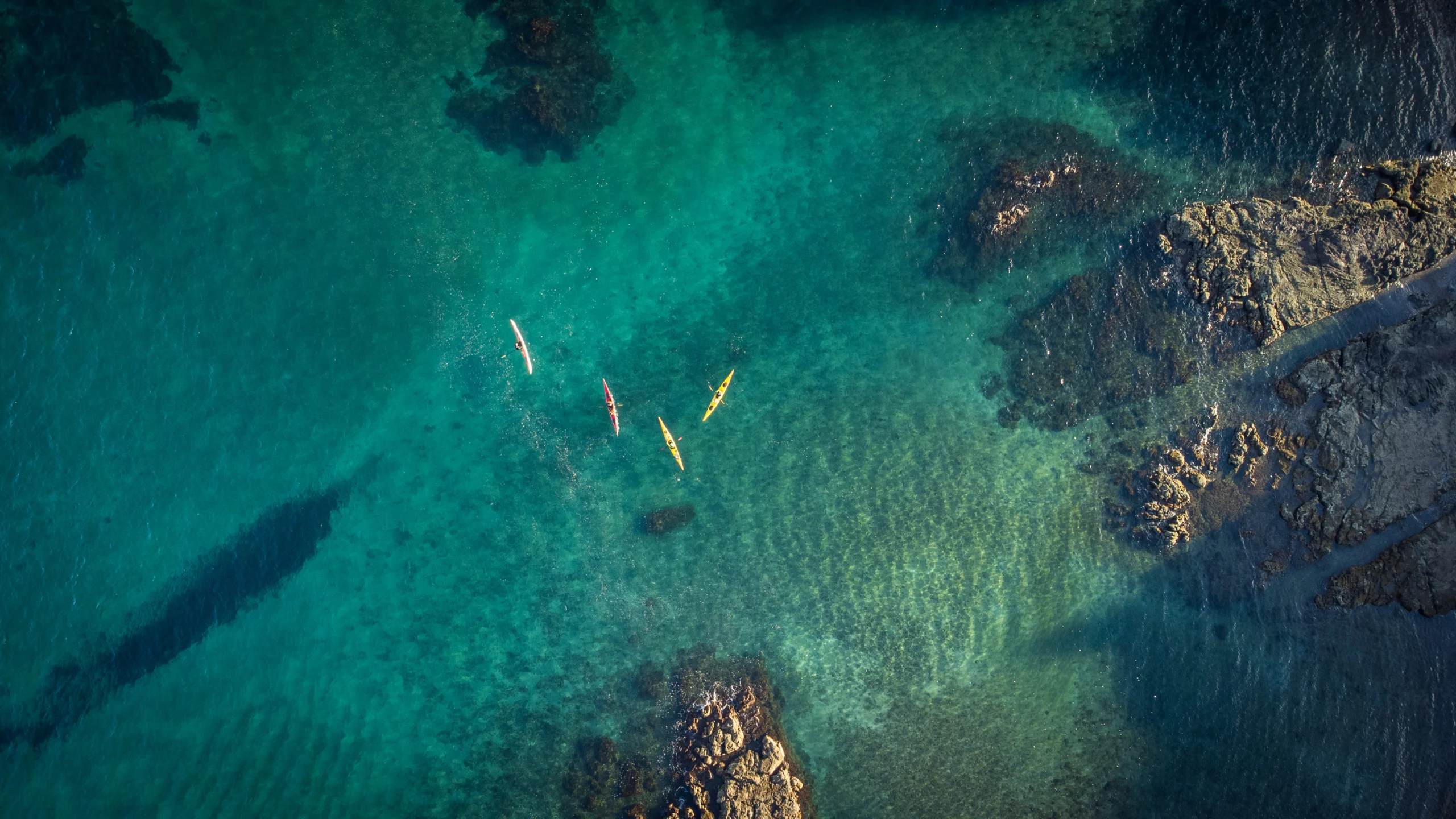 four kayaks float on an emerald ocean
