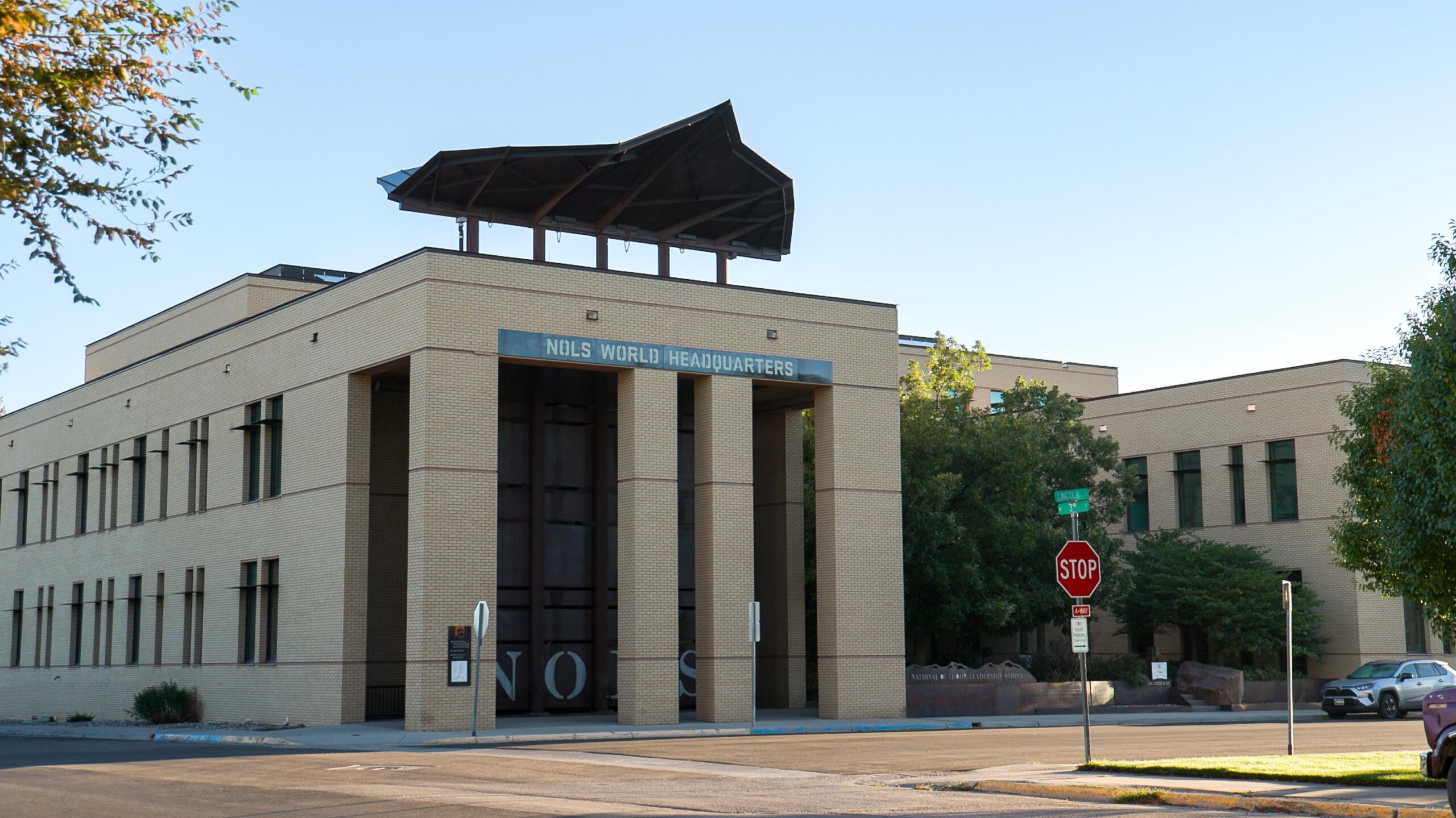 a two-story building on a corner lot. the building has three pillars in the front and a large sculpture on the top.