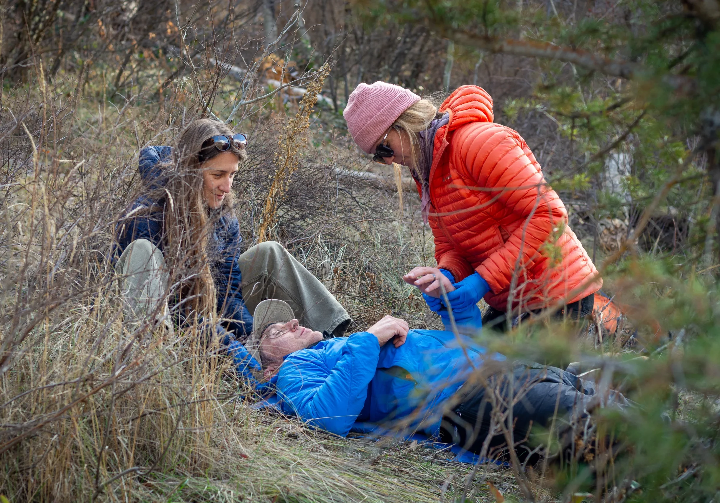 two woman in puffy jackets help a person lying on the ground